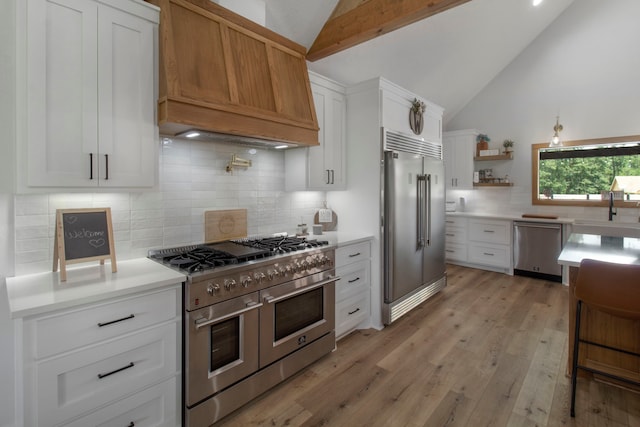 kitchen featuring premium appliances, custom exhaust hood, white cabinetry, light hardwood / wood-style floors, and sink