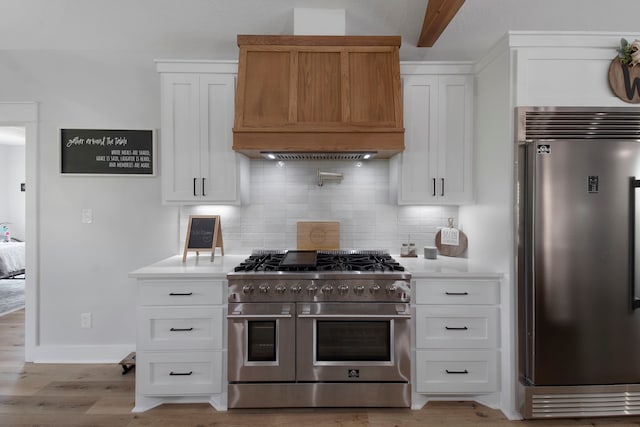 kitchen featuring white cabinetry, custom exhaust hood, premium appliances, light hardwood / wood-style floors, and decorative backsplash