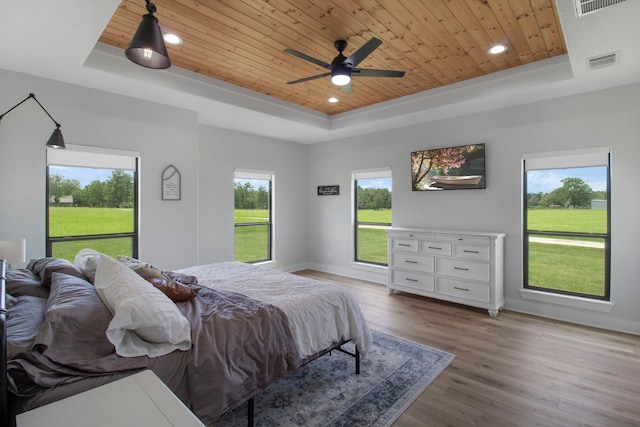 bedroom featuring ceiling fan, light hardwood / wood-style floors, a raised ceiling, multiple windows, and wooden ceiling