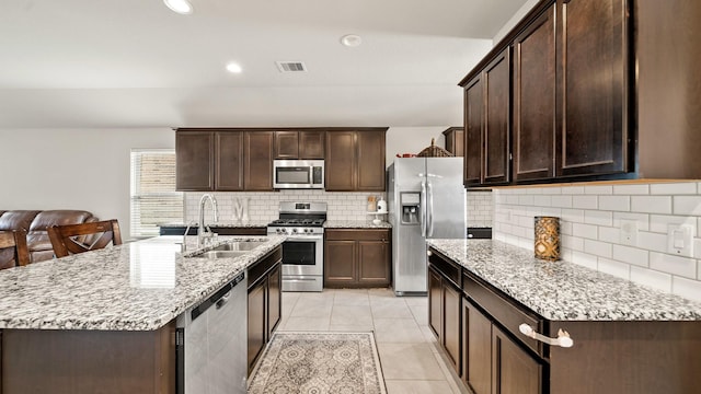 kitchen featuring sink, light stone countertops, light tile patterned floors, an island with sink, and stainless steel appliances