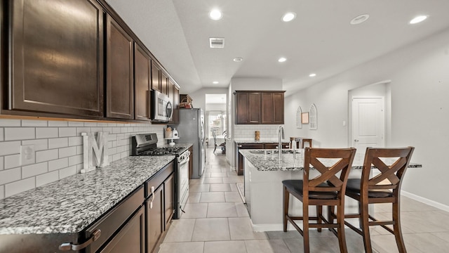 kitchen with a breakfast bar, a kitchen island with sink, light tile patterned floors, light stone counters, and stainless steel appliances