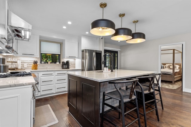 kitchen featuring dark hardwood / wood-style flooring, an island with sink, decorative backsplash, stainless steel fridge, and sink