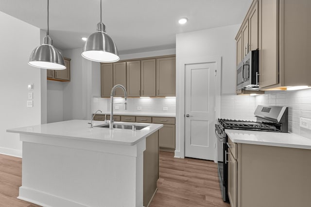 kitchen with sink, appliances with stainless steel finishes, light hardwood / wood-style floors, an island with sink, and decorative light fixtures