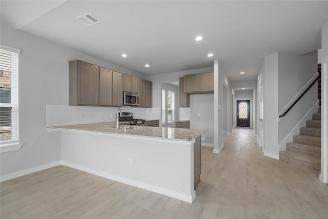 kitchen featuring backsplash, light stone counters, kitchen peninsula, stainless steel appliances, and light hardwood / wood-style flooring