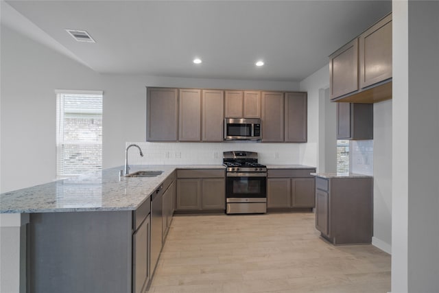 kitchen featuring sink, stainless steel appliances, light stone countertops, decorative backsplash, and kitchen peninsula