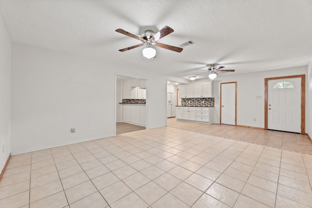 unfurnished living room featuring a textured ceiling, ceiling fan, and light tile patterned floors