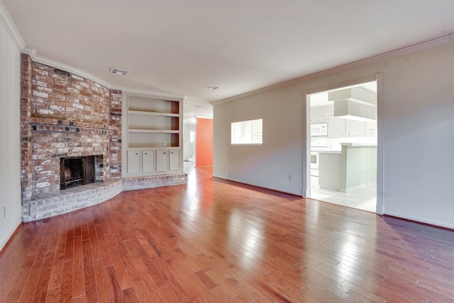 unfurnished living room with built in shelves, light wood-type flooring, a fireplace, and crown molding