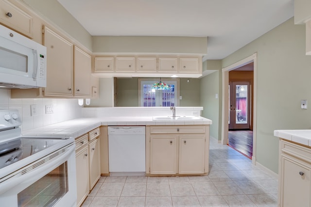 kitchen with light tile patterned floors, tile countertops, backsplash, white appliances, and sink