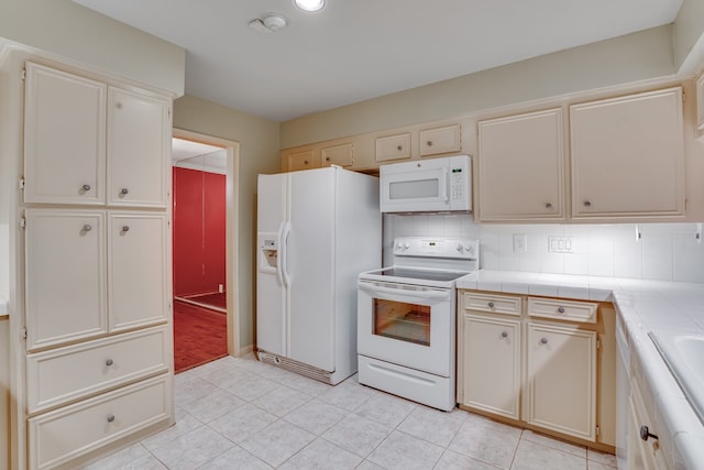 kitchen with light tile patterned floors, tile countertops, cream cabinetry, tasteful backsplash, and white appliances