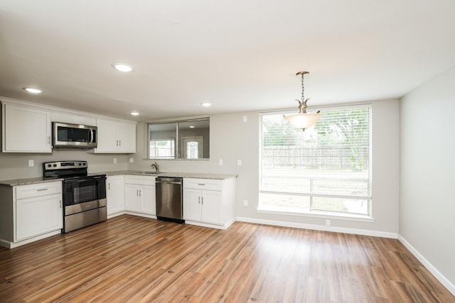 kitchen with light stone countertops, pendant lighting, white cabinets, appliances with stainless steel finishes, and light hardwood / wood-style flooring