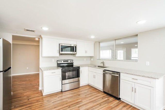 kitchen with appliances with stainless steel finishes, white cabinetry, light stone counters, and sink