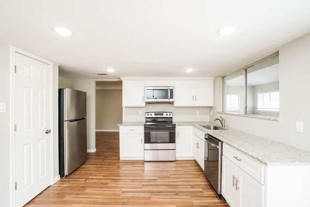 kitchen with light stone countertops, white cabinets, appliances with stainless steel finishes, sink, and light wood-type flooring