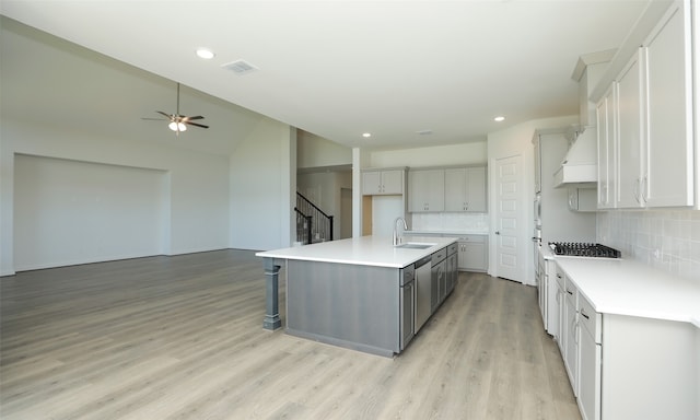 kitchen featuring sink, decorative backsplash, an island with sink, light hardwood / wood-style floors, and custom range hood