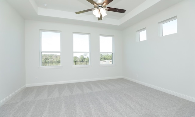 carpeted empty room with ceiling fan, a raised ceiling, and a wealth of natural light