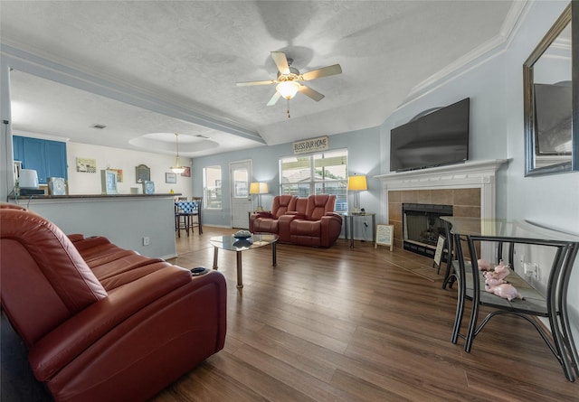 living room featuring dark wood-type flooring, a textured ceiling, a raised ceiling, ceiling fan, and a tiled fireplace