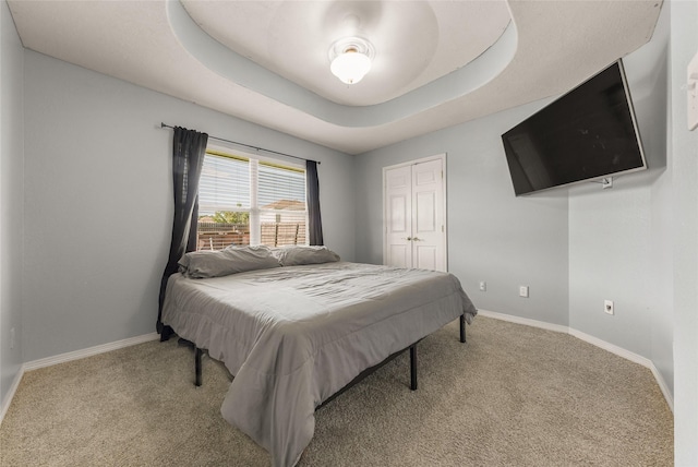 carpeted bedroom featuring a raised ceiling and a closet