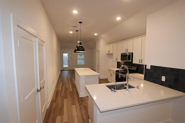 kitchen featuring backsplash, a center island with sink, hanging light fixtures, white cabinetry, and stainless steel appliances