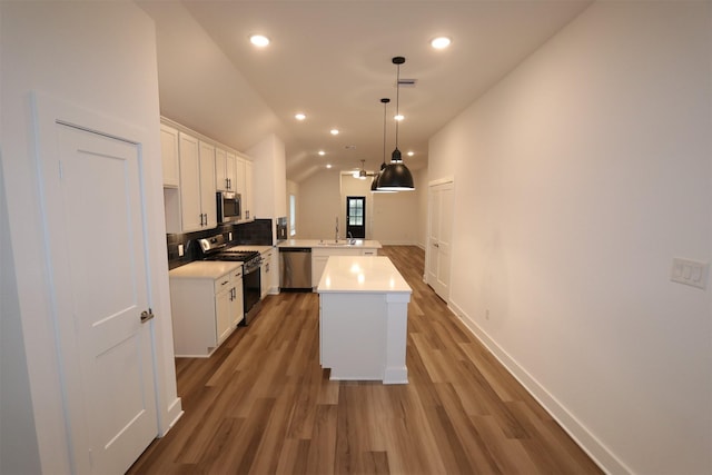 kitchen with stainless steel appliances, kitchen peninsula, pendant lighting, vaulted ceiling, and white cabinets