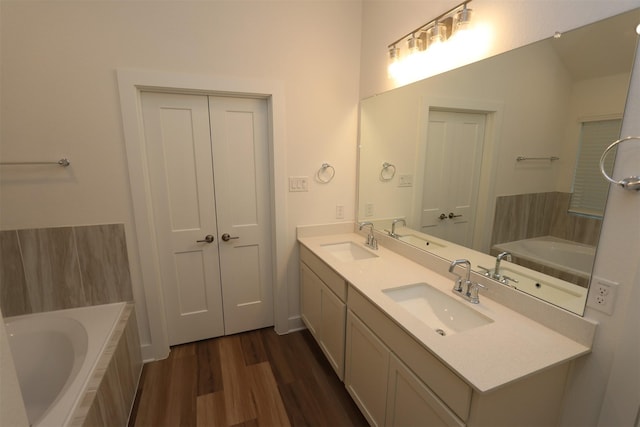 bathroom with hardwood / wood-style floors, vanity, and tiled tub