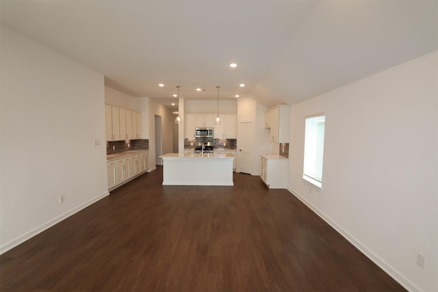 kitchen with hanging light fixtures, stainless steel appliances, dark hardwood / wood-style flooring, backsplash, and a center island with sink