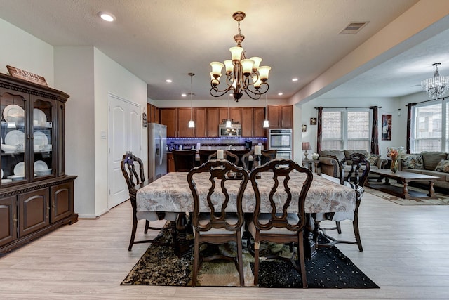 dining room with a notable chandelier, light hardwood / wood-style floors, and a textured ceiling