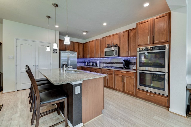 kitchen featuring an island with sink, decorative light fixtures, appliances with stainless steel finishes, a breakfast bar, and light wood-type flooring