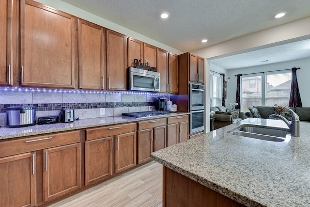 kitchen with light hardwood / wood-style floors, a textured ceiling, sink, stainless steel appliances, and light stone countertops