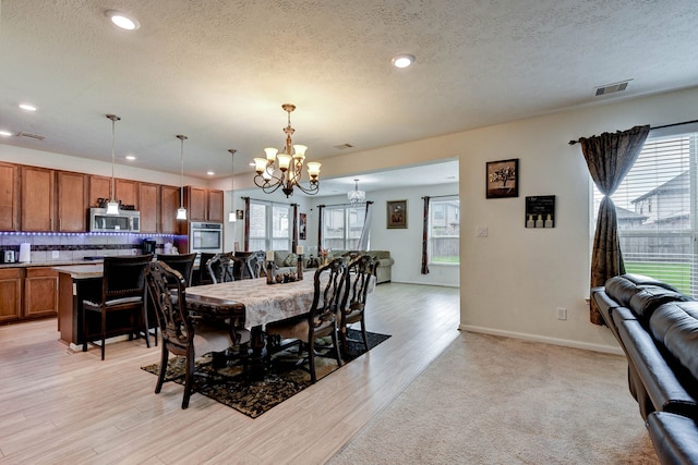 dining area with a notable chandelier, light wood-type flooring, and a textured ceiling