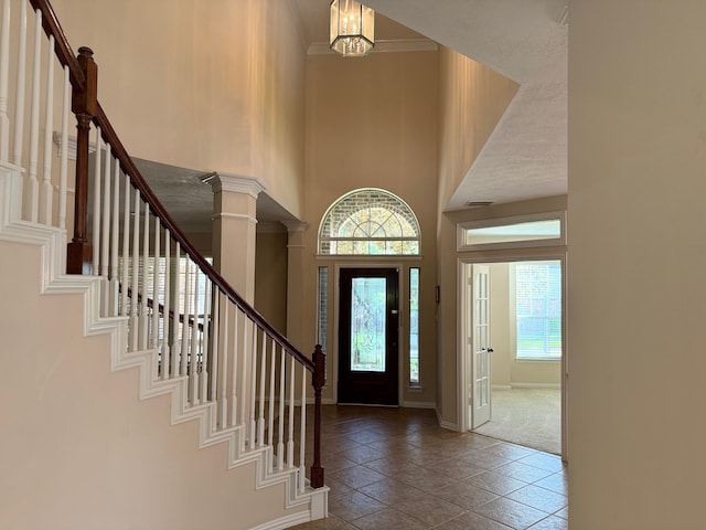 tiled foyer entrance with a notable chandelier, decorative columns, and a high ceiling