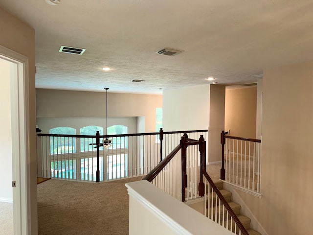 corridor with a notable chandelier, carpet flooring, and a textured ceiling