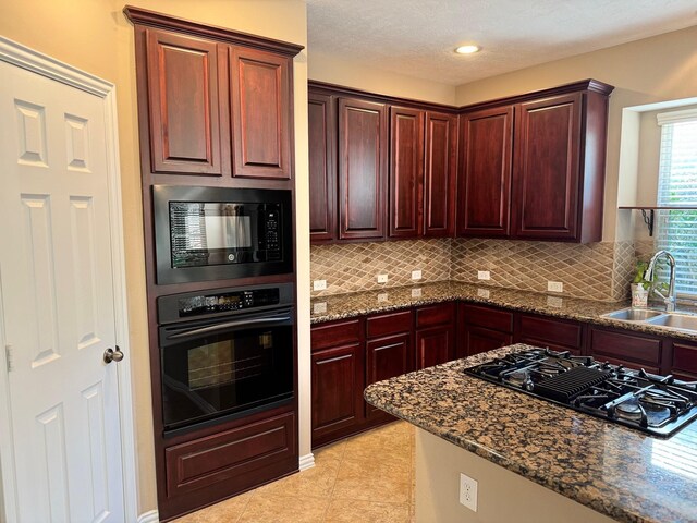 kitchen with light tile patterned flooring, dark stone countertops, tasteful backsplash, black appliances, and sink