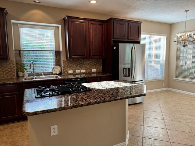 kitchen with light tile patterned flooring, dark stone counters, stainless steel refrigerator with ice dispenser, decorative backsplash, and black gas cooktop