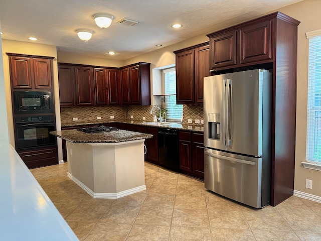 kitchen with dark stone counters, a center island, black appliances, decorative backsplash, and sink