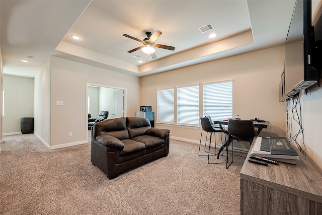 living room with a tray ceiling, ceiling fan, and carpet flooring