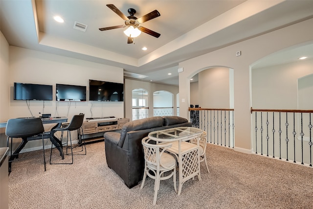 living room with a raised ceiling, ceiling fan, and light colored carpet