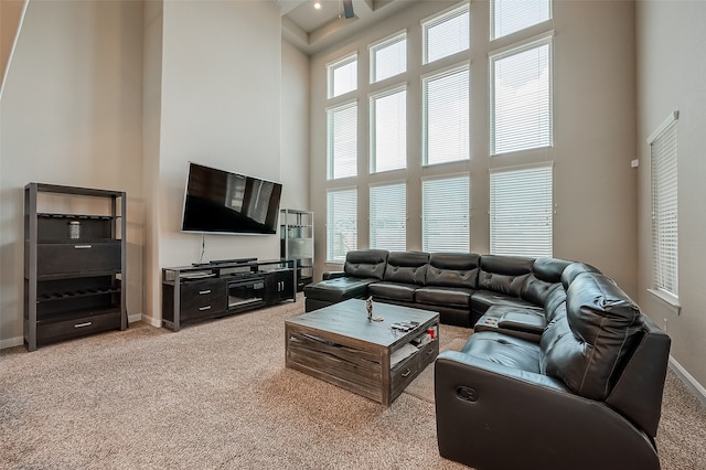 carpeted living room with ceiling fan, a towering ceiling, and plenty of natural light