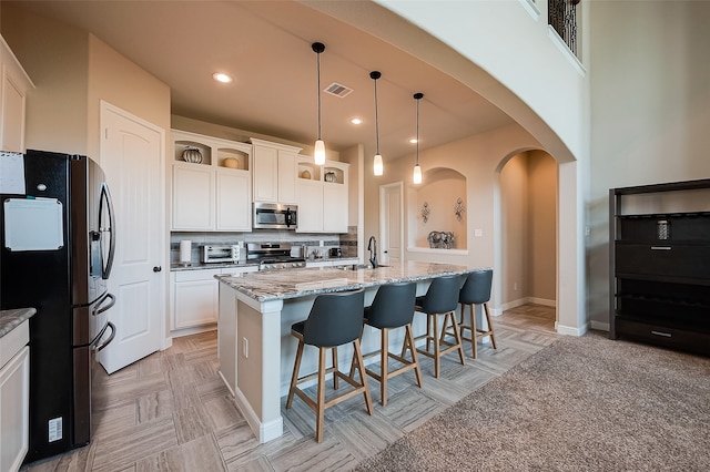 kitchen featuring appliances with stainless steel finishes, hanging light fixtures, tasteful backsplash, white cabinets, and a center island with sink