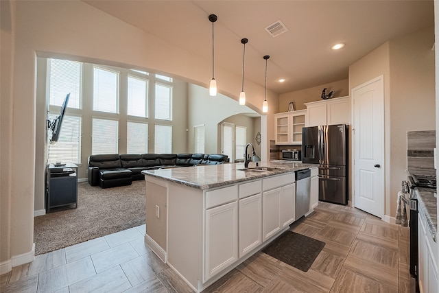 kitchen featuring light carpet, stainless steel appliances, white cabinetry, and a center island with sink