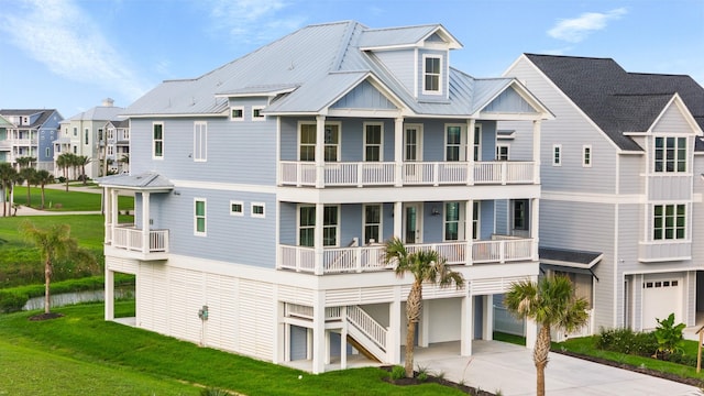 rear view of property with an attached garage, a lawn, metal roof, a balcony, and driveway