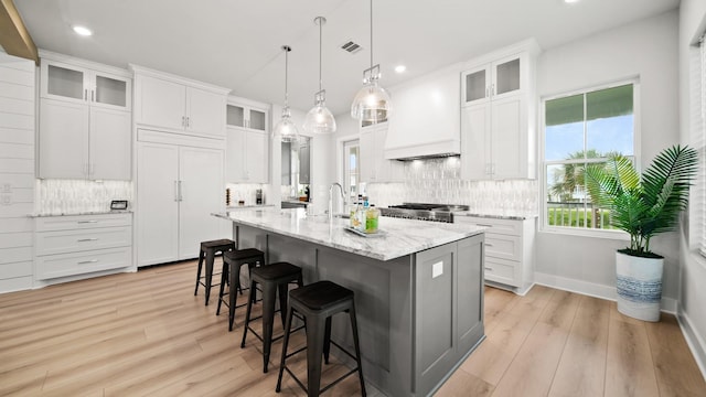 kitchen featuring paneled fridge, a center island with sink, custom exhaust hood, a kitchen bar, and tasteful backsplash