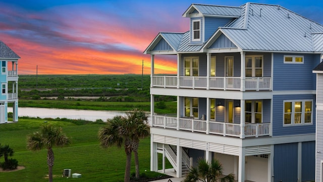 rear view of house with a water view, a lawn, a standing seam roof, metal roof, and a balcony