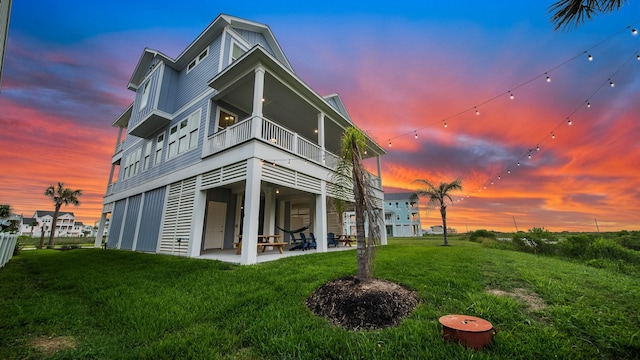 back of property at dusk with a balcony, a patio area, and a lawn