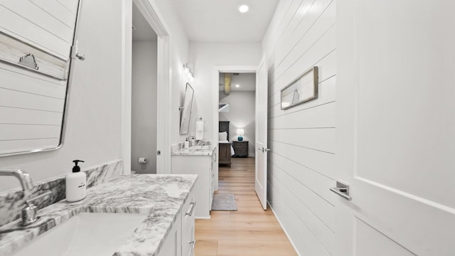 ensuite bathroom with connected bathroom, wood finished floors, and vanity