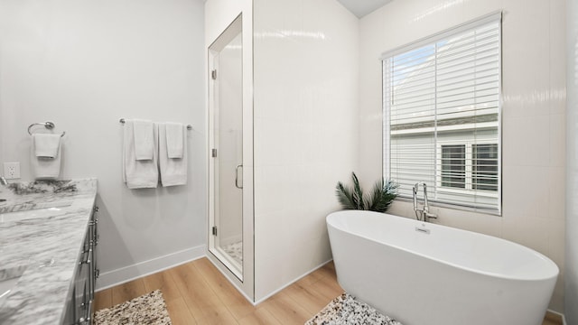 bathroom featuring vanity, wood finished floors, baseboards, a freestanding bath, and a shower stall