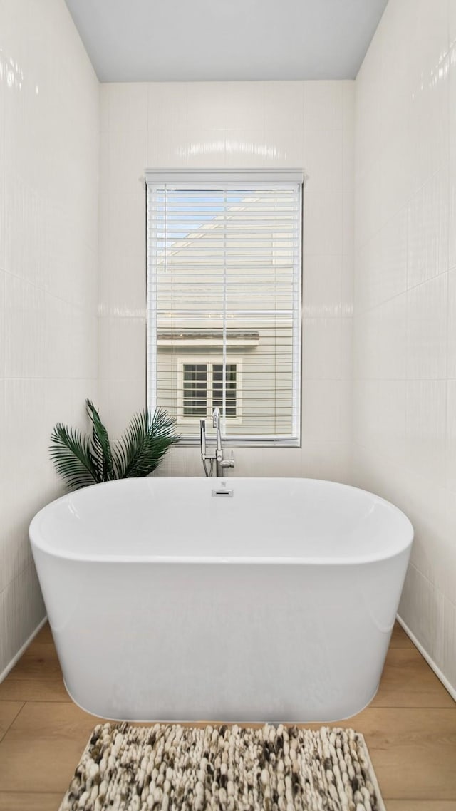 bathroom with tile walls, a soaking tub, and wood finished floors