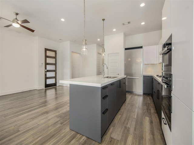 kitchen with pendant lighting, sink, wall oven, white cabinets, and a center island with sink