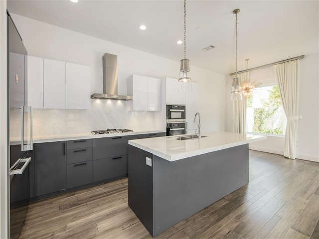 kitchen with pendant lighting, a kitchen island with sink, white cabinetry, stainless steel gas cooktop, and wall chimney exhaust hood