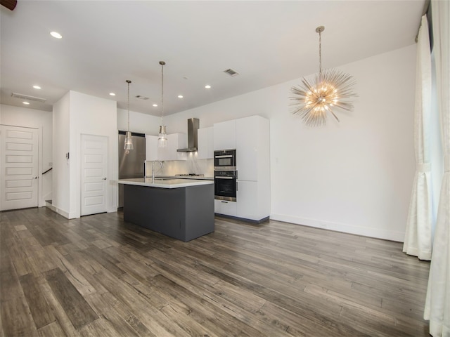 kitchen featuring wall chimney exhaust hood, sink, white cabinetry, decorative light fixtures, and an island with sink