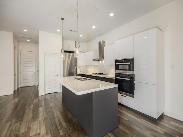 kitchen featuring sink, white cabinetry, a center island with sink, stainless steel appliances, and wall chimney range hood