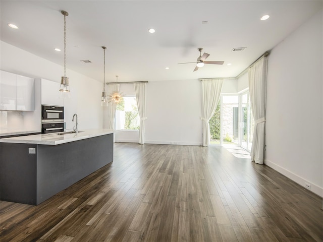 kitchen with sink, white cabinetry, dark hardwood / wood-style floors, a center island with sink, and decorative light fixtures